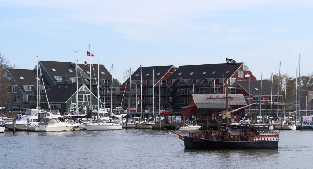 Annapolis Harbor featuring sailboats, a pirate ship, and historical buildings. 